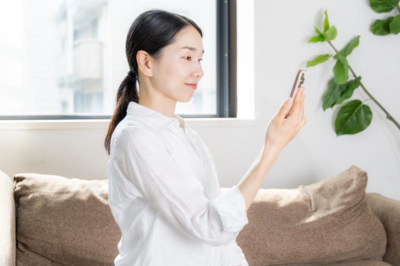 スマホを正しい姿勢で操作する女性。画面を目線の高さまで上げ、背筋を伸ばして首への負担を最小限に抑えている様子。